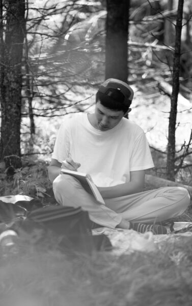 gap year program student sitting on the ground by trees looking at a notebook